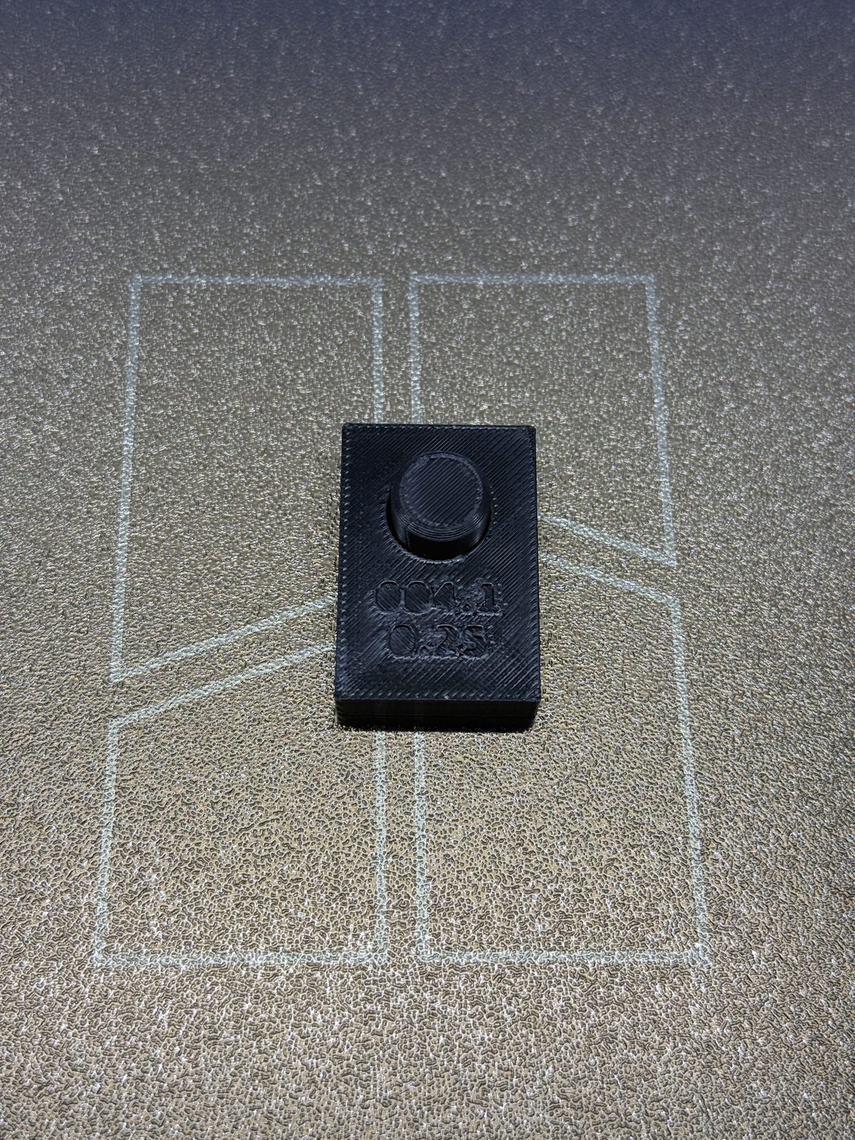 BRIM-004 iteration 1 assembled on the printer bed: the gauge block, debossed 004.1 and 0.25, seated flush on the peg plate, the dark PETG peg standing proud through the bore.