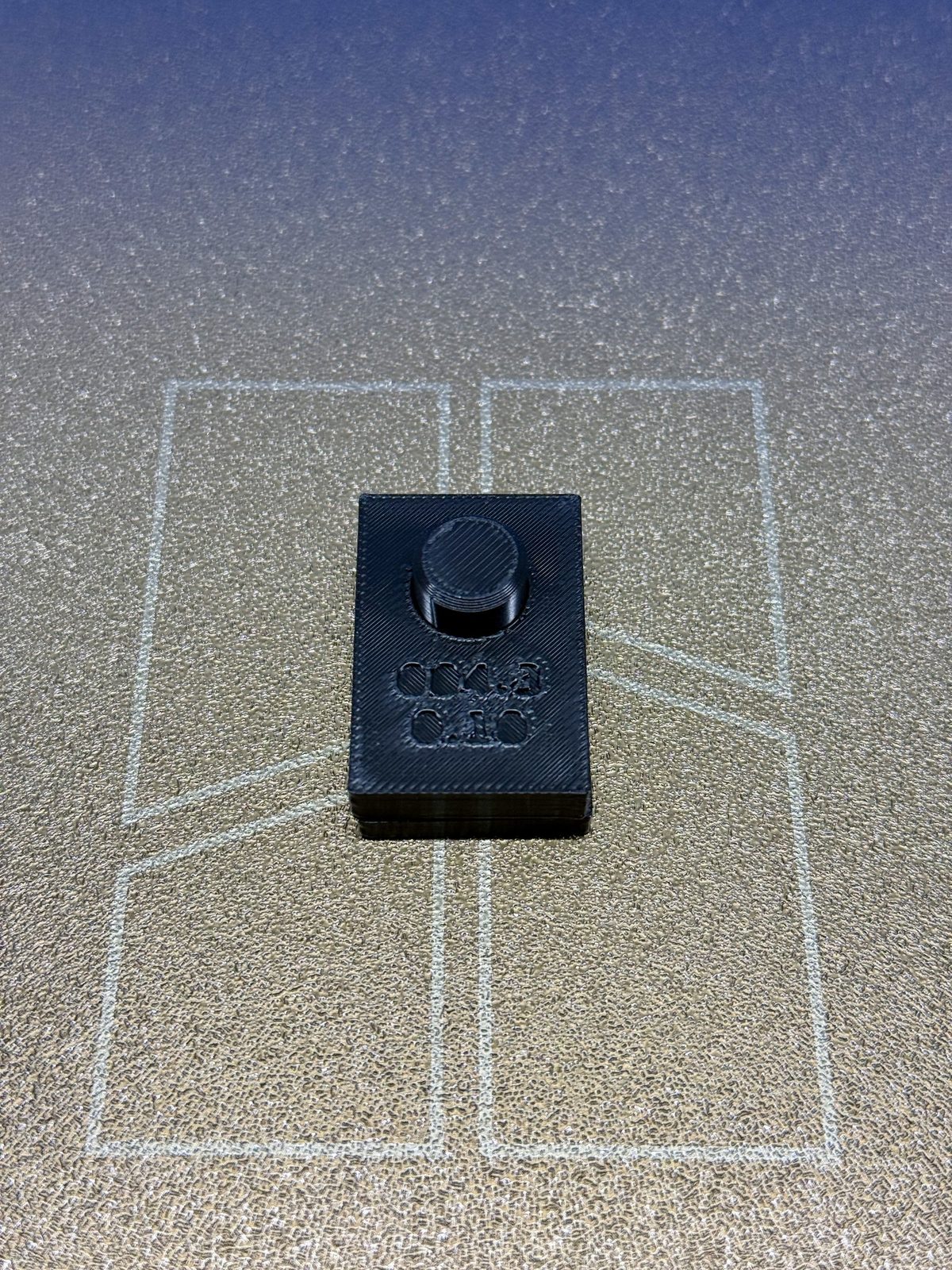 BRIM-004 iteration 3 assembled on the printer bed: the gauge block, debossed 004.3 and 0.10, seated on the peg plate with the dark PETG peg standing proud through the bore.