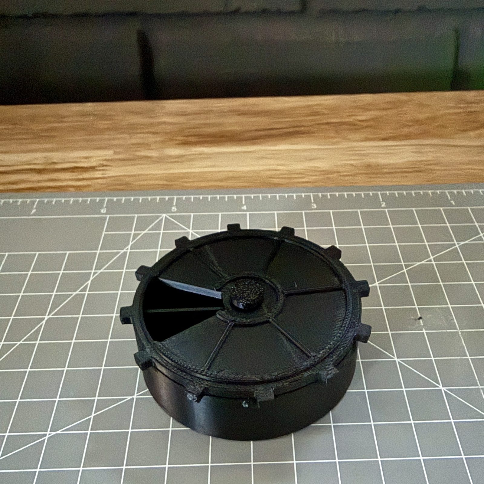 The rev B printed set assembled on a green cutting mat: cup, gear-toothed vault-door lid seated flush, pin seated in the centre hub.